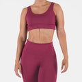 Woman wearing a maroon sports bra and leggings on a white background
